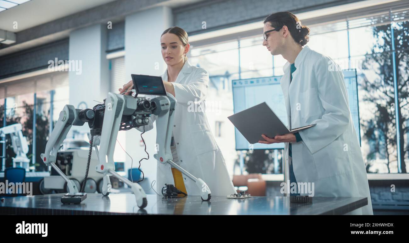 Male Project Manager and Female Machinery Operator Collaborate on a Mobile Robot Animal Project, Using Laptop Computer. Two Professional Engineers Brainstorming, Discussing Futuristic AI Pet Stock Photo