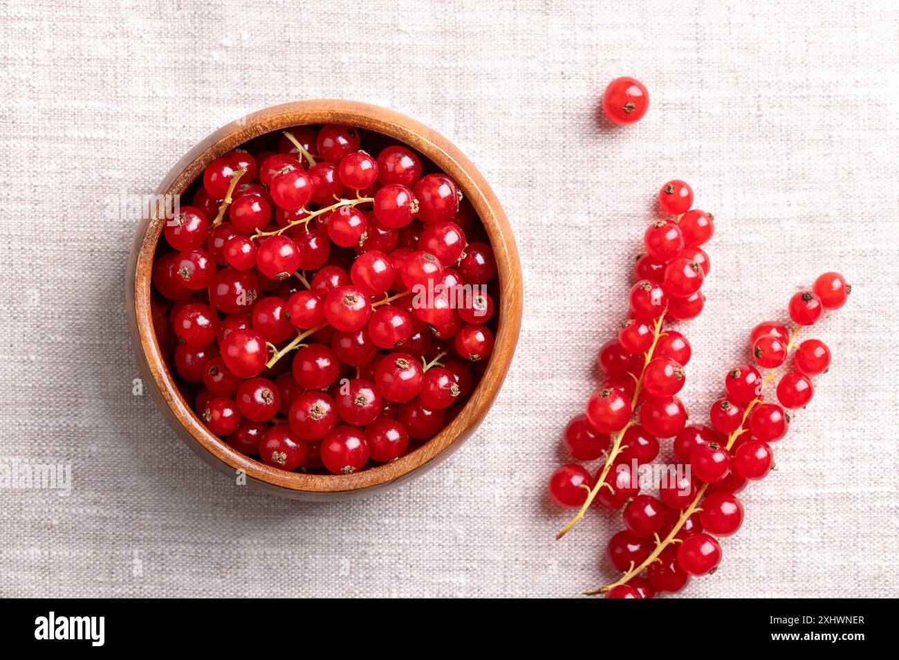 Red currant berries, fresh ripe and raw redcurrants in a wooden bowl on linen fabric. Ready to eat spherical edible fruits of Ribes rubrum. Stock Photo