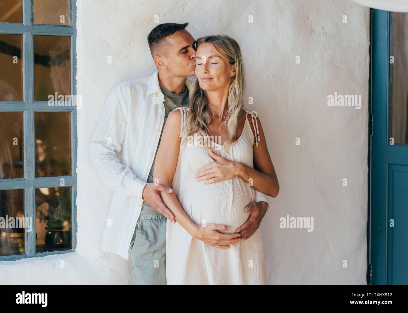 Handsome man hugs and kisses his beautiful pregnant wife while standing ...