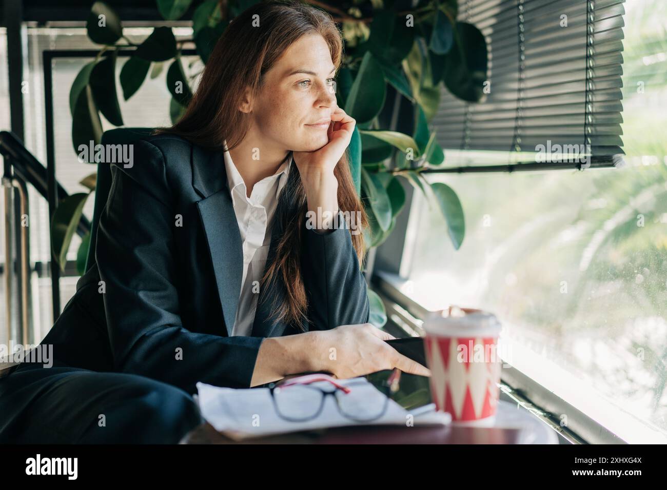 A young beautiful woman in a business suit sitting in a cafe waiting for a corporate meeting. Stock Photo