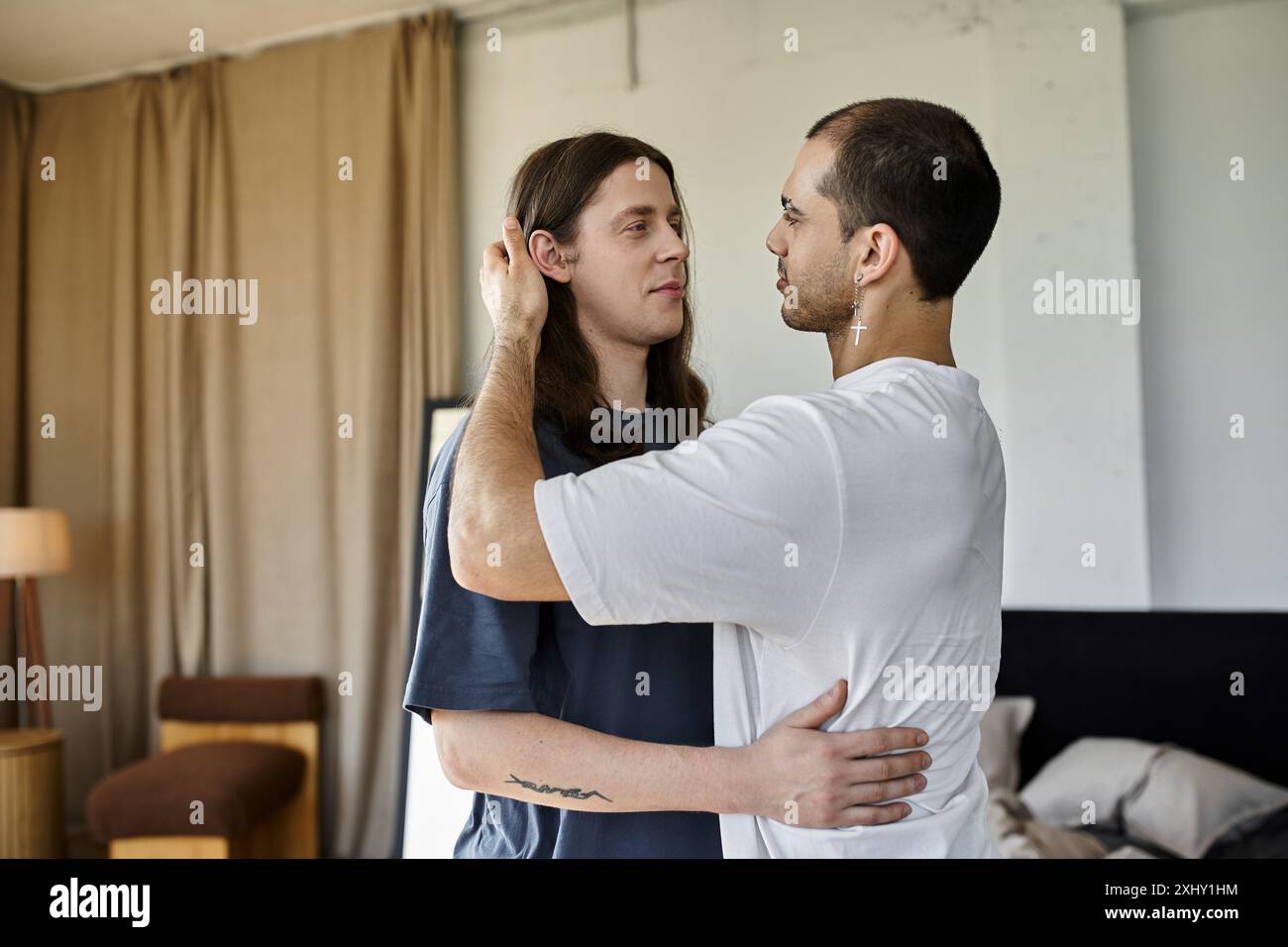 Stand Close A young gay couple stands close together in a bedroom, sharing a tender ...