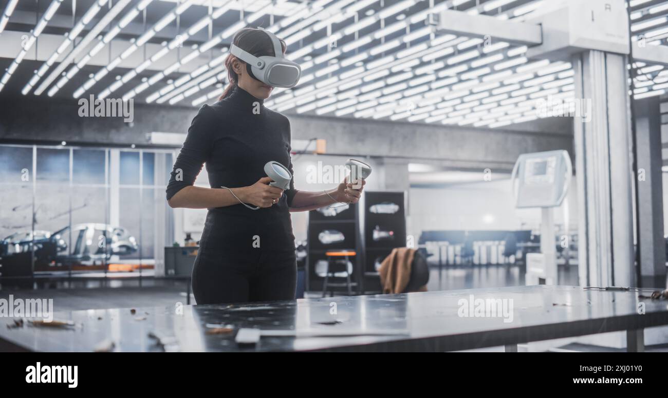 Young Female Wearing a Virtual Reality Headset and Using Controllers at Work in a Technology Research and Development Office. VR Software Developer Programming a Game or Augmented Reality Application Stock Photo