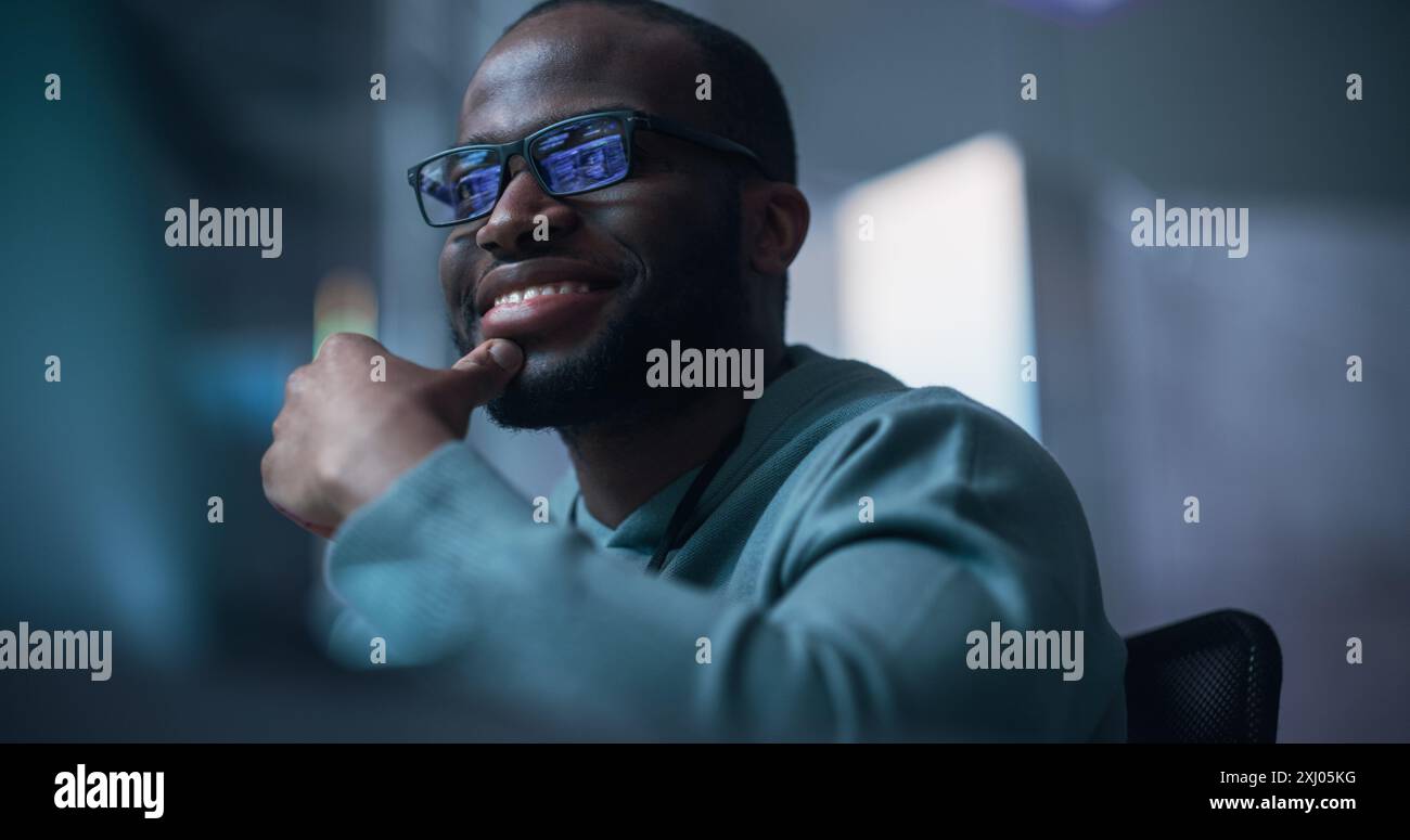 Close Up Of Black Male Developer Smiling Happily After Successfully Typing on Computer a Functioning Software Code. Professional Programmer Creating Mobile App, Screen Display Reflected on his Glasses Stock Photo