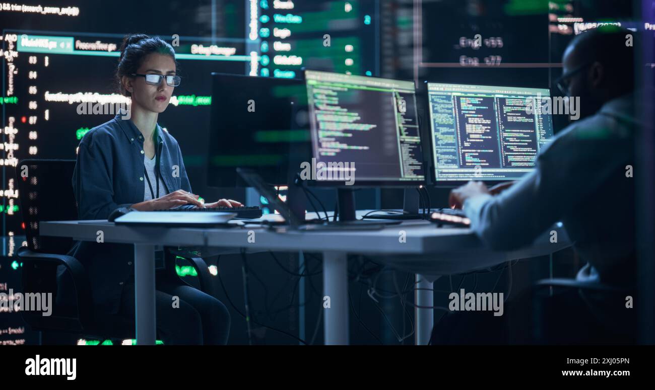 Diverse Young Man and Woman Working on Desktop Computers, Surrounded by Big Screens Displaying Code Prompts. Professional Computer Engineers Developing Autonomous Algorithm for Generative AI. Stock Photo
