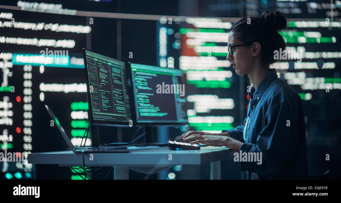 Female Developer Thinking and Typing on Computer, Surrounded by Big Screens Showing Coding Language. Professional Programmer Working in an Office, Running Coding Tests. Futuristic Programming Stock Photo
