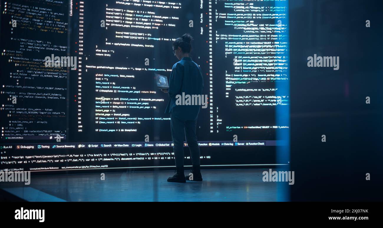 Portrait of Young Woman Working on Laptop Computer, Looking at Big Digital Screen Displaying Back-end Code Lines. Professional Programmer Developing a Big Data Interface Software Project Concept. Stock Photo