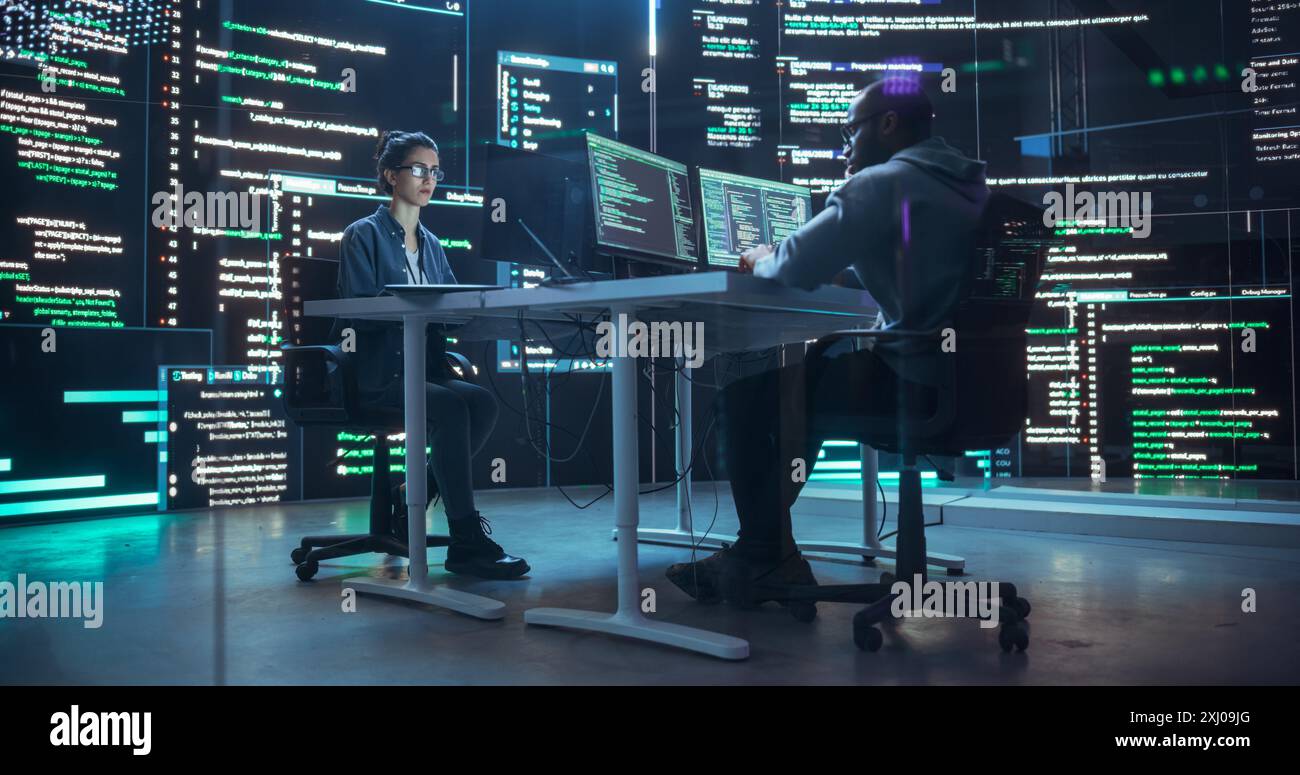 Diverse Young Man and Woman Working on Desktop Computers, Surrounded by Big Screens Displaying Code Lines. Professional Computer Engineers Developing Autonomous Algorithm for Generative AI Stock Photo