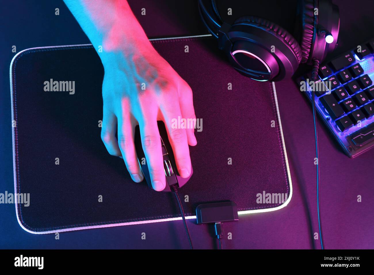 Gamer using modern wired computer mouse at dark table in neon lights ...