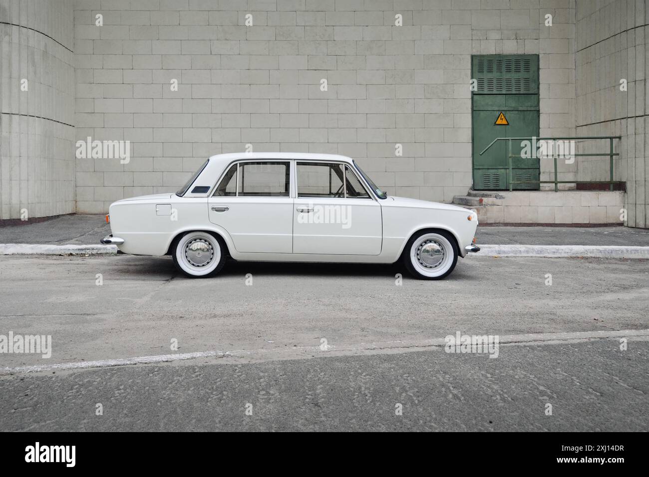 White old sedan in front of ivory tiled building wall. Side