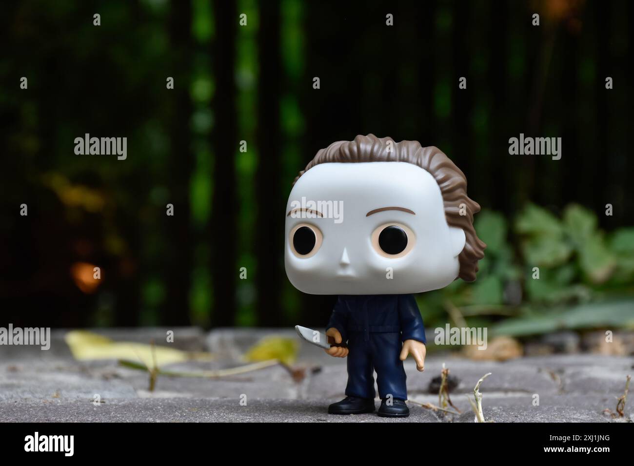 Funko Pop action figure of serial killer Michael Myers from horror movies Halloween. Dark yard, black fence, shadows, moody green background. Stock Photo