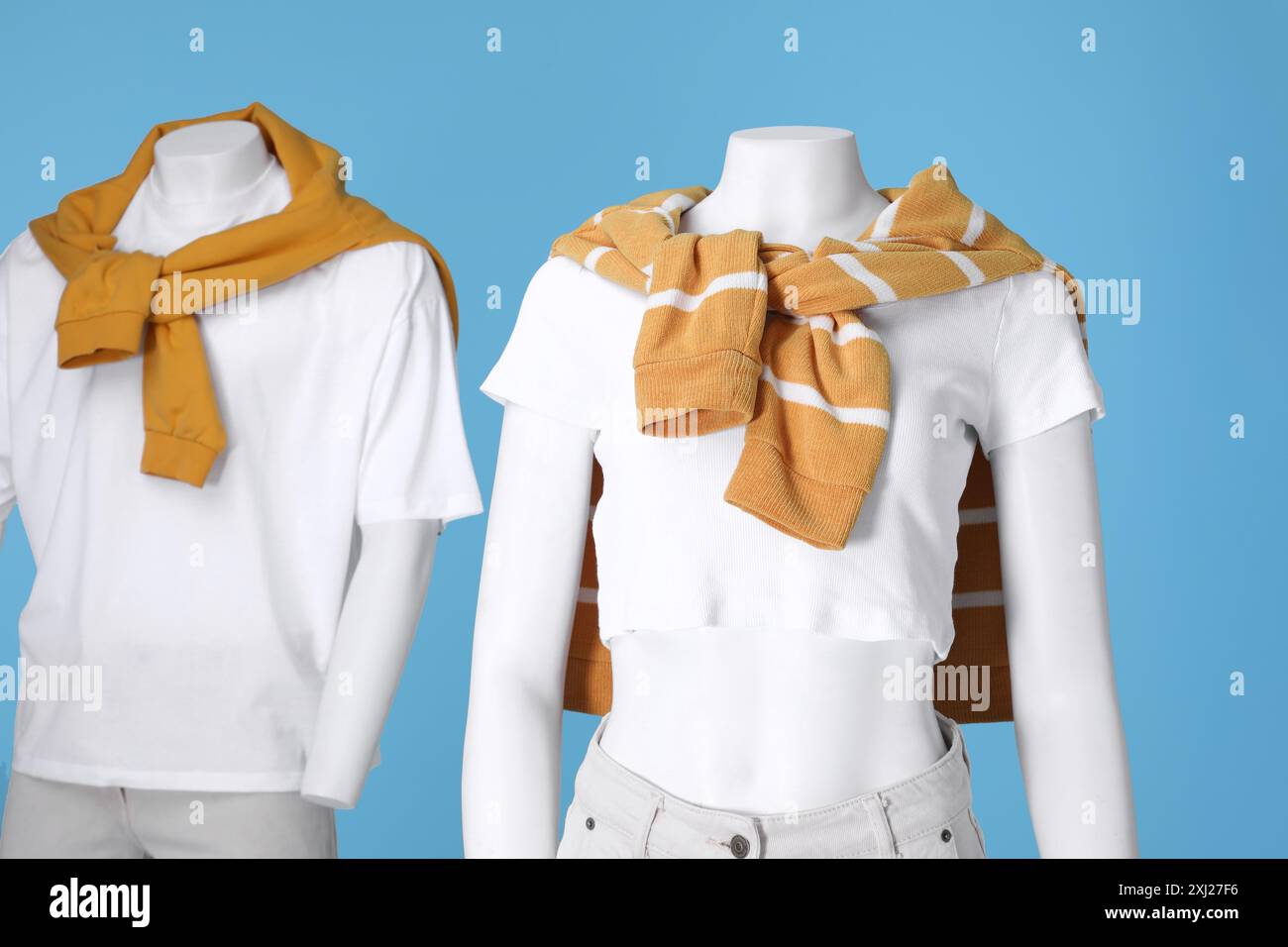 Female and male mannequins dressed in white t-shirts, stylish jeans and orange sweaters on light blue background Stock Photo