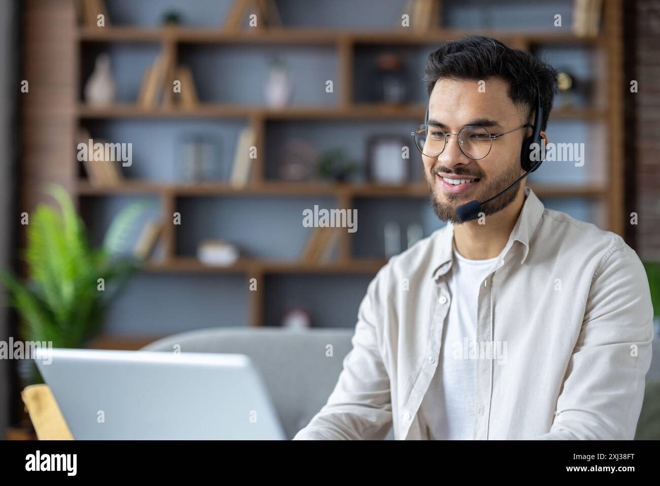 Smiling customer service representative working remotely from home office with headset and laptop. Professional support agent providing customer care while maintaining a positive , friendly attitude Stock Photo