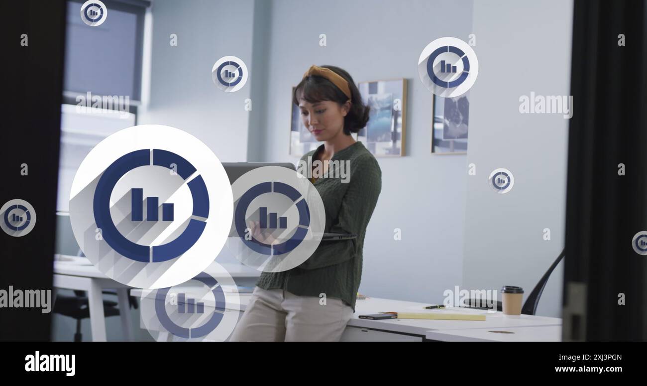 Image of multiple bar graph icons floating over asian woman using laptop at office. Computer interface and business data technology concept Stock Photo