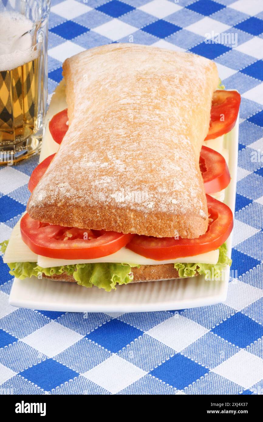 Close-up of an italian panino (sandwich) with freshly baked ciabatta bread, lettuce, cheese and tomato. In the background a glass of beer. Selective Stock Photo
