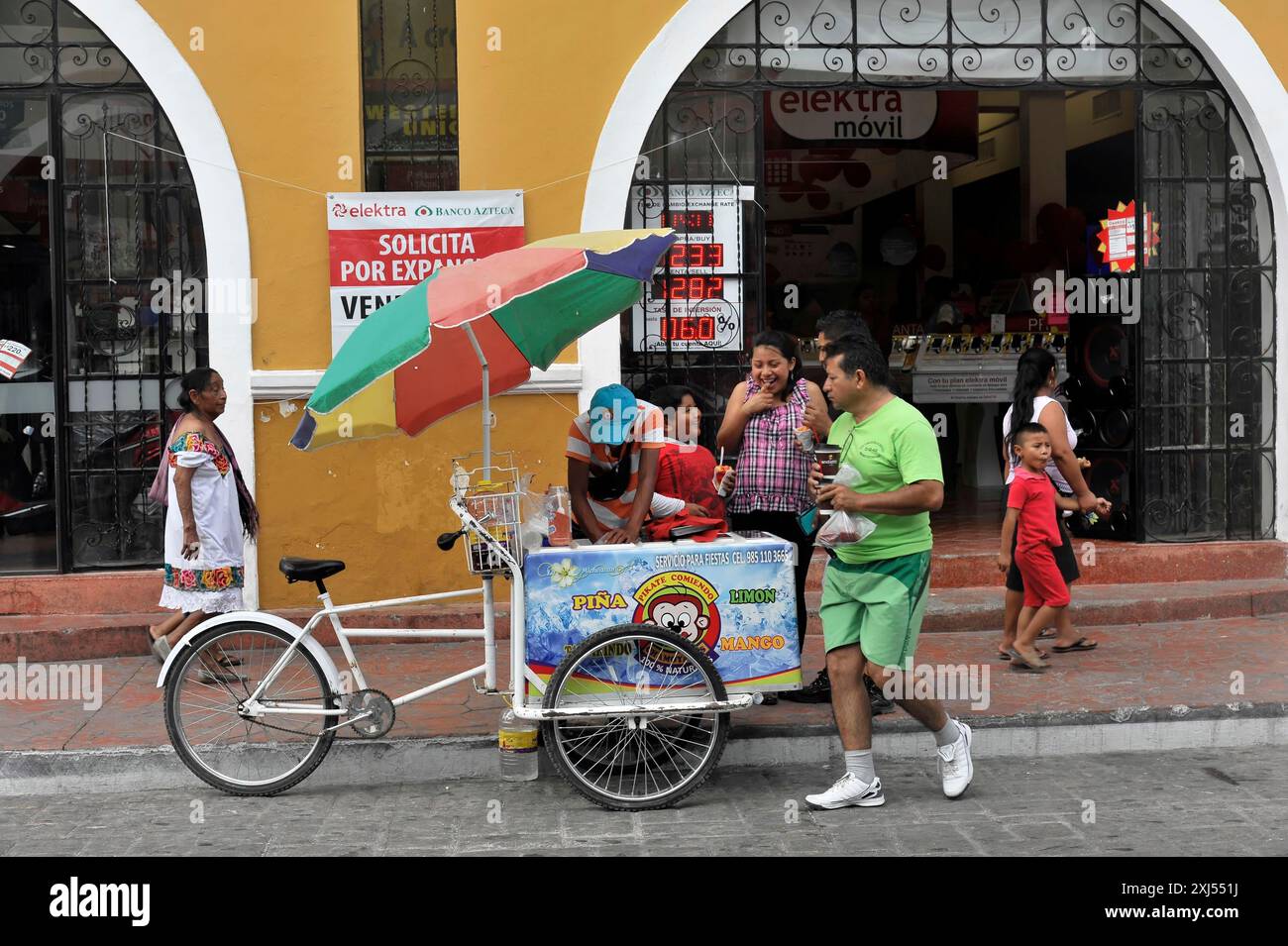 Merida, Yucatan, Mexico, Central America, Street scene with an ice cream vendor and customers, including a colourful parasol and busy street scene Stock Photo