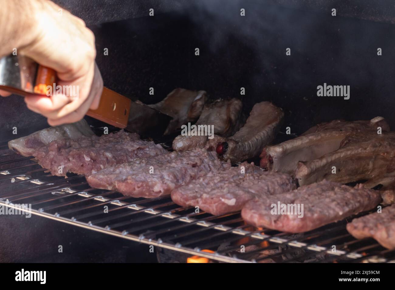 Grilling in action: A chef expertly flips sizzling meats on a smoky barbecue grill, capturing the essence of outdoor cooking and summertime culinary a Stock Photo