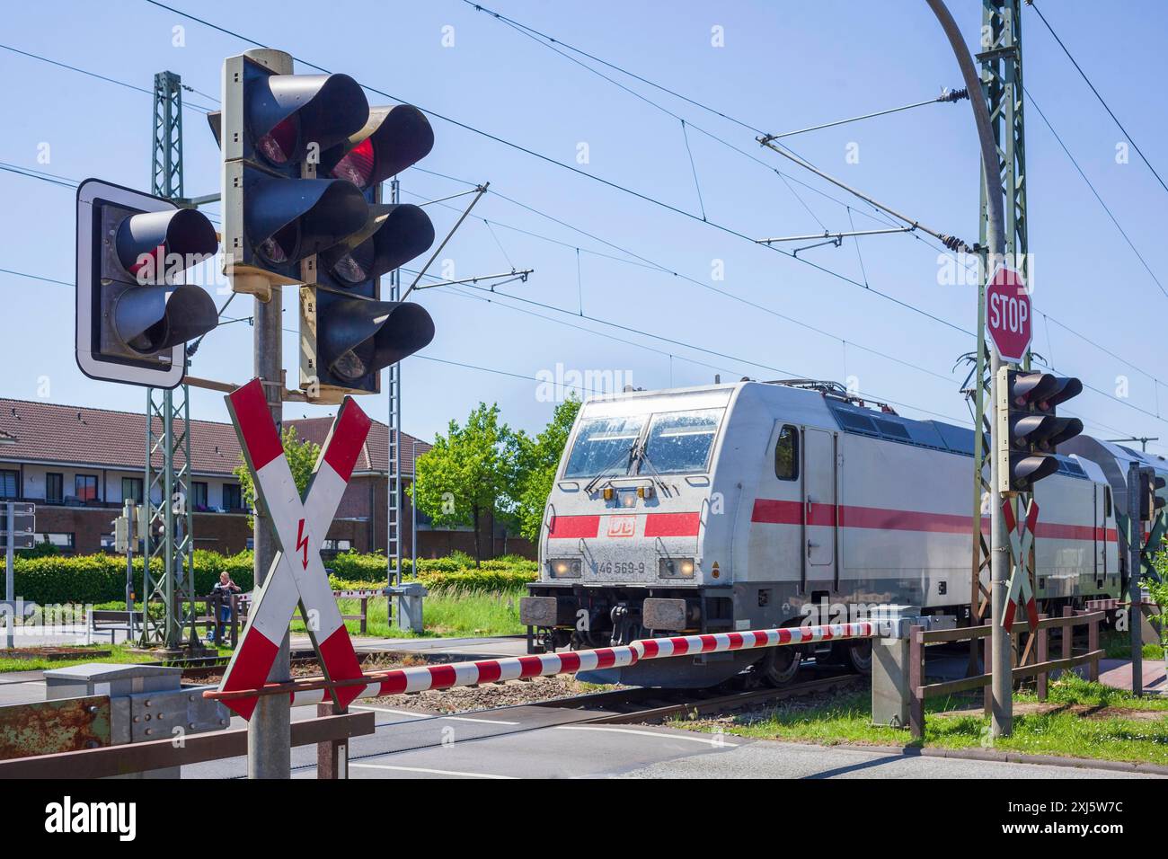 Gated railway crossing with closed barriers and local train, Bad Zwischenahn, Lower Saxony, Germany Stock Photo