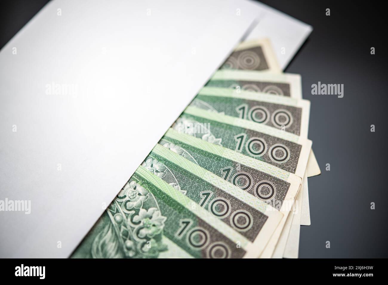 Close-up view of Polish Zlotys (PLN) emerging from a plain, unmarked white envelope, symbolizing gifts, laundering, and illicit financial activities. Stock Photo