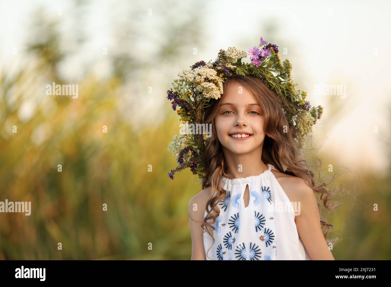 Happy little girl wearing wreath made of beautiful flowers outdoors ...