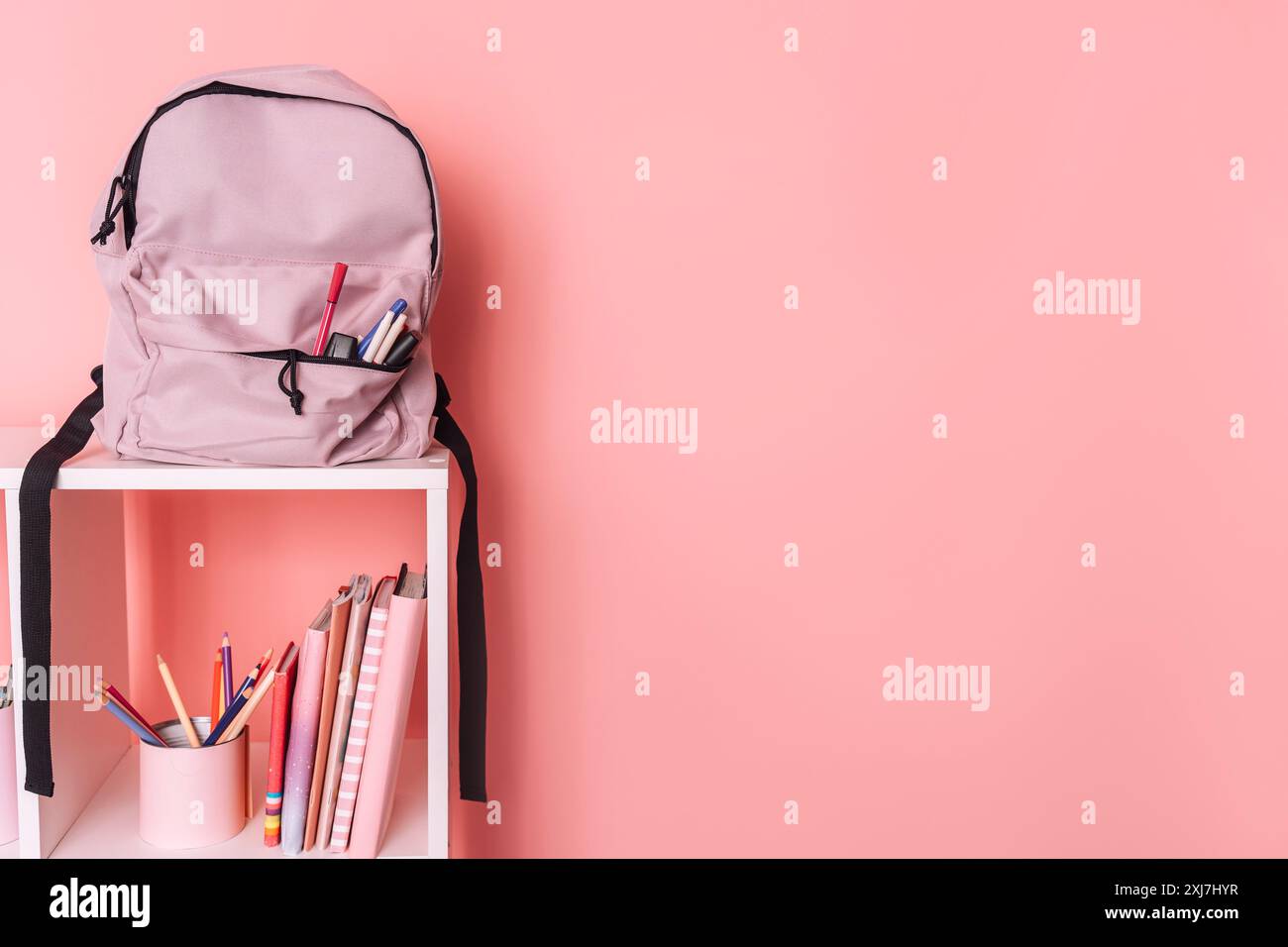 There are school supplies and a backpack on white shelves against a pink background Stock Photo