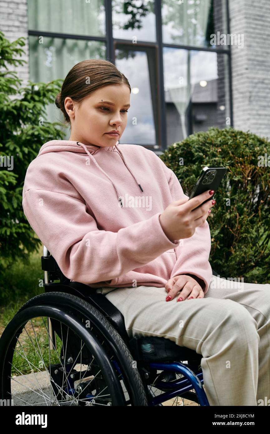 A young woman with a disability sits in a wheelchair, using her phone ...