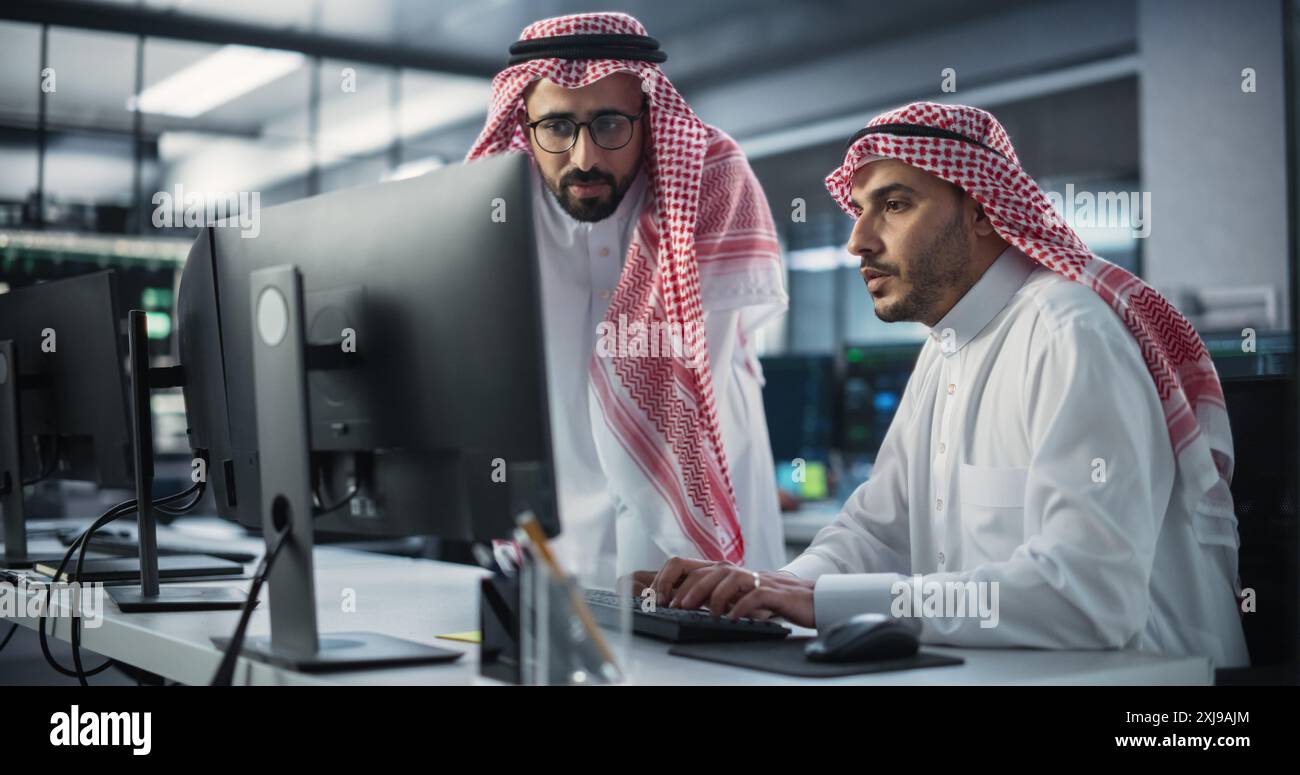 Two Multiethnic Arab Colleagues Having a Conversation While Busy Working on a Software Development Project. Engineer Talking with a Middle Eastern Project Manager. Teamwork in Technology Laboratory Stock Photo
