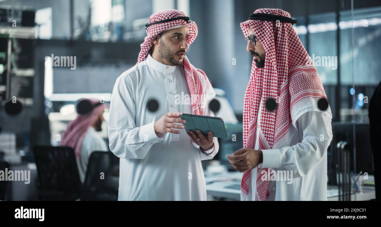 Two Multiethnic Arab Colleagues Having a Conversation While Busy Working on a Software Development Project. Engineer Talking with a Middle Eastern Project Manager, Using Tablet Computer in Office Stock Photo