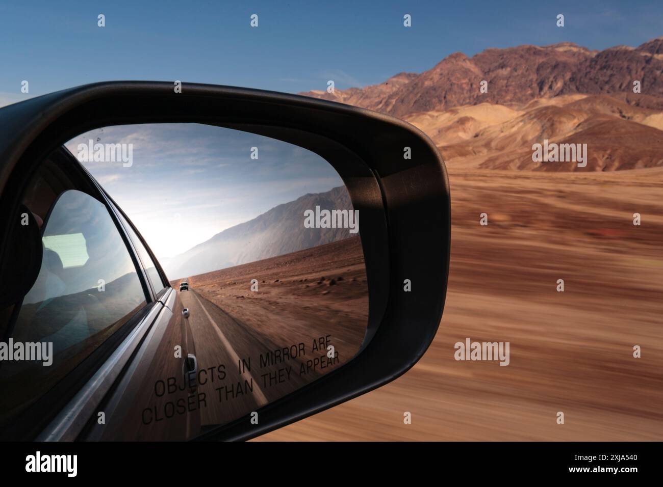 Side mirror view of a car, view of the road behind in a desert national ...