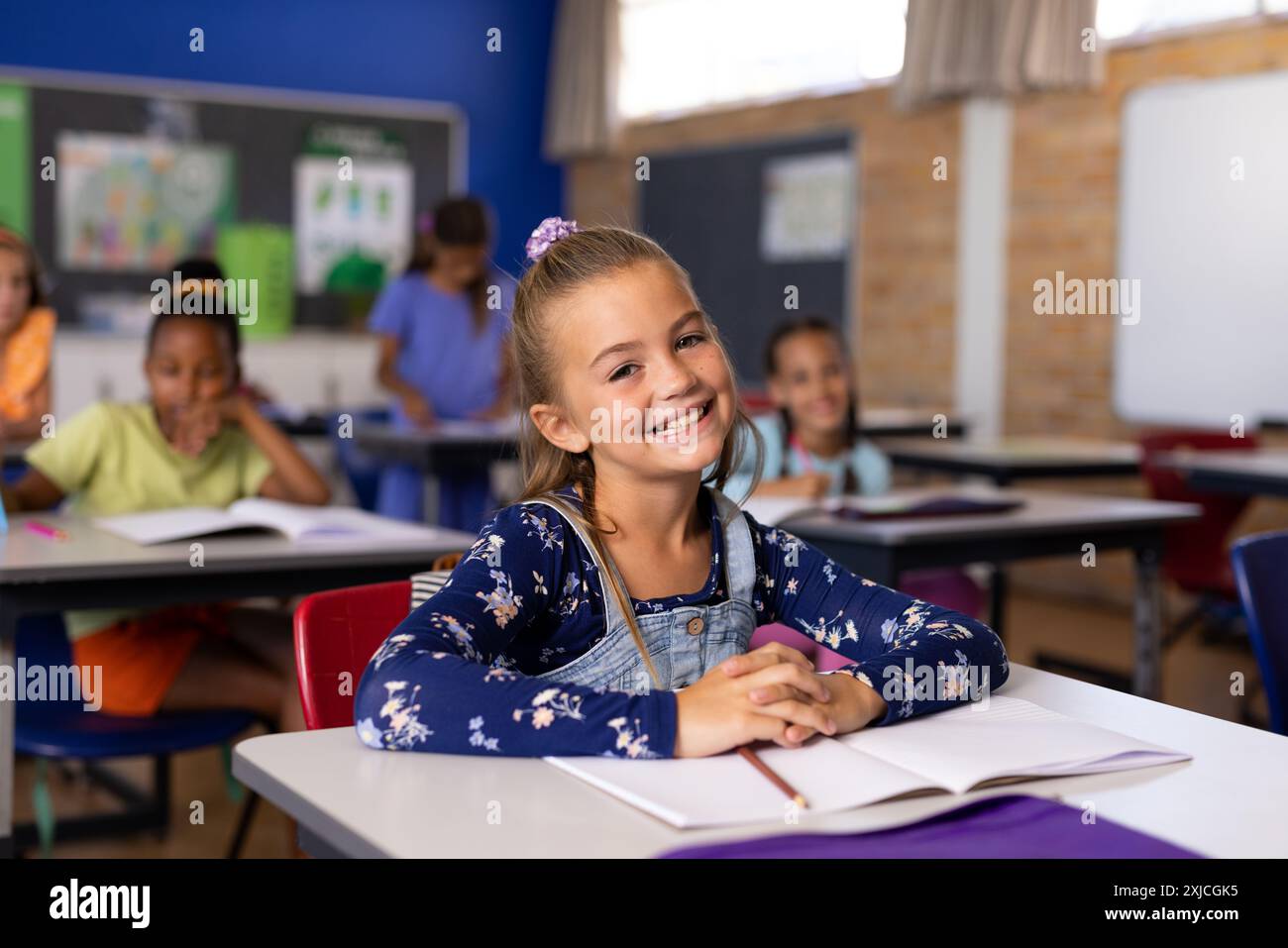 Portrait of cute smiling caucasian schoolgirl with book on desk ...