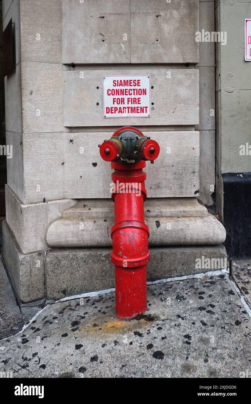 Siamese connection fire hydrant for the fire department, a red standpipe against a stone skyscraper footing in on 5th Avenue, New York City Stock Photo