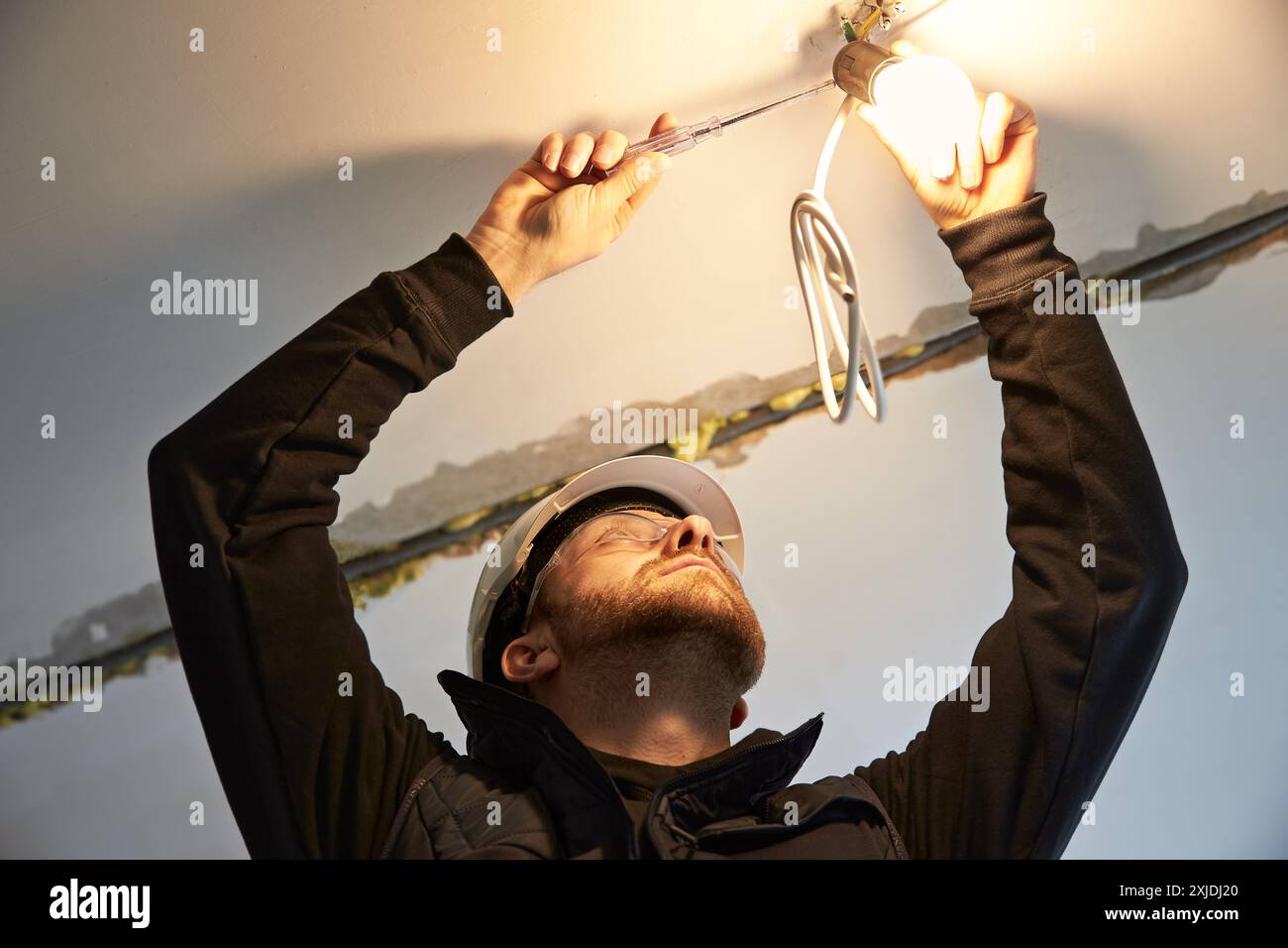 Portrait of male electrician, focused on wiring a temporary light bulb ...