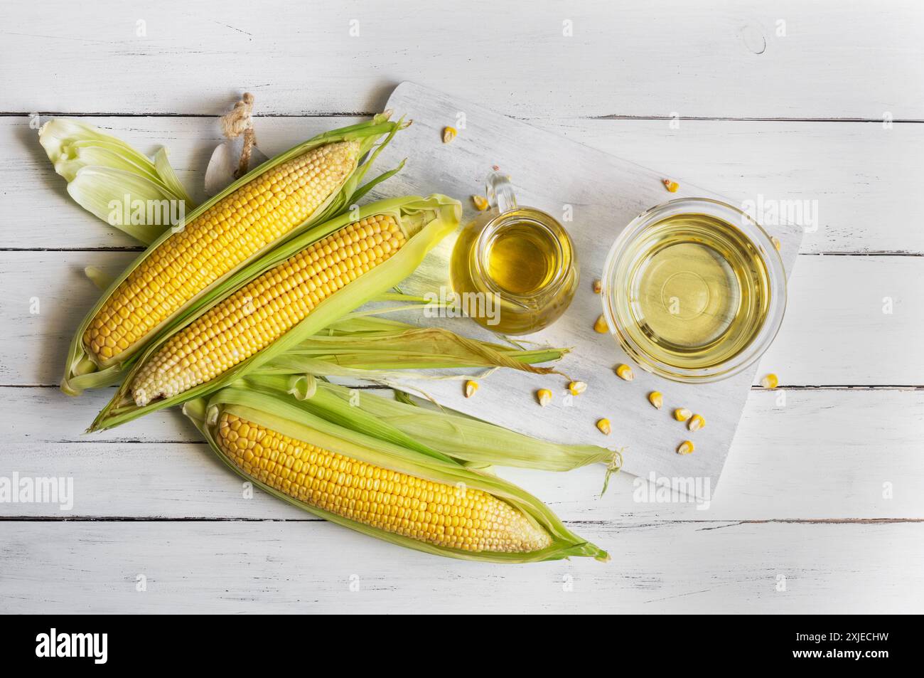 Corn oil in glass bowl with fresh ripe corn cobs on rustic table ...