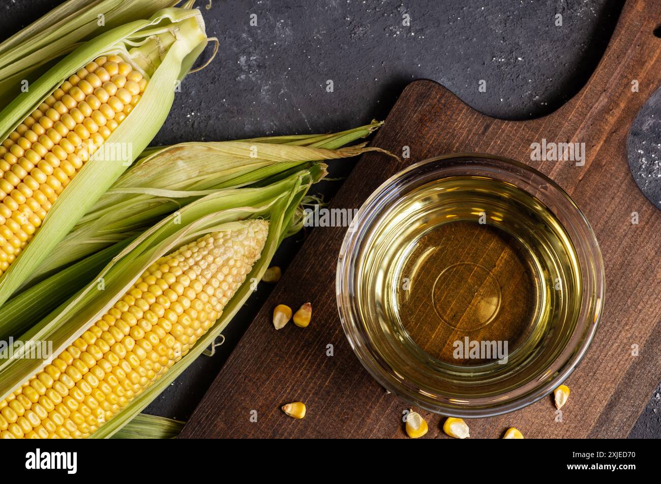 Corn oil in glass bowl with fresh ripe corn cobs on rustic table ...