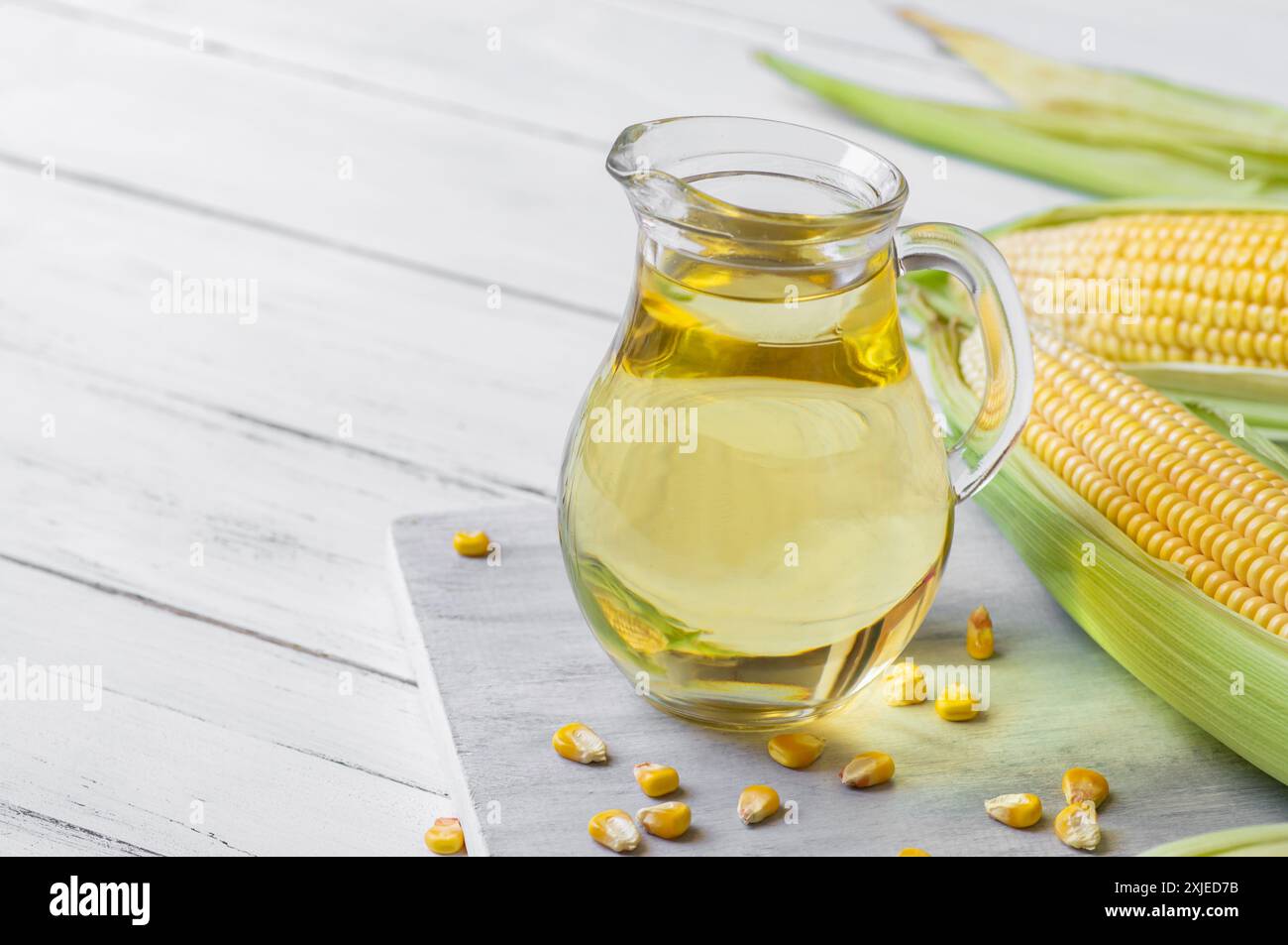 Corn oil in glass bowl with fresh ripe corn cobs on rustic table ...