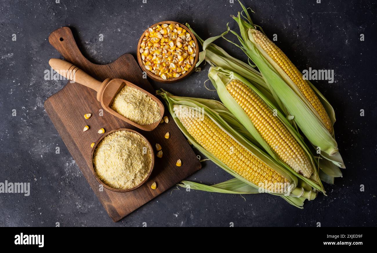 Corn flour in wooden bowl or spoon with fresh corn cobs, kernels on rustic table Stock Photo