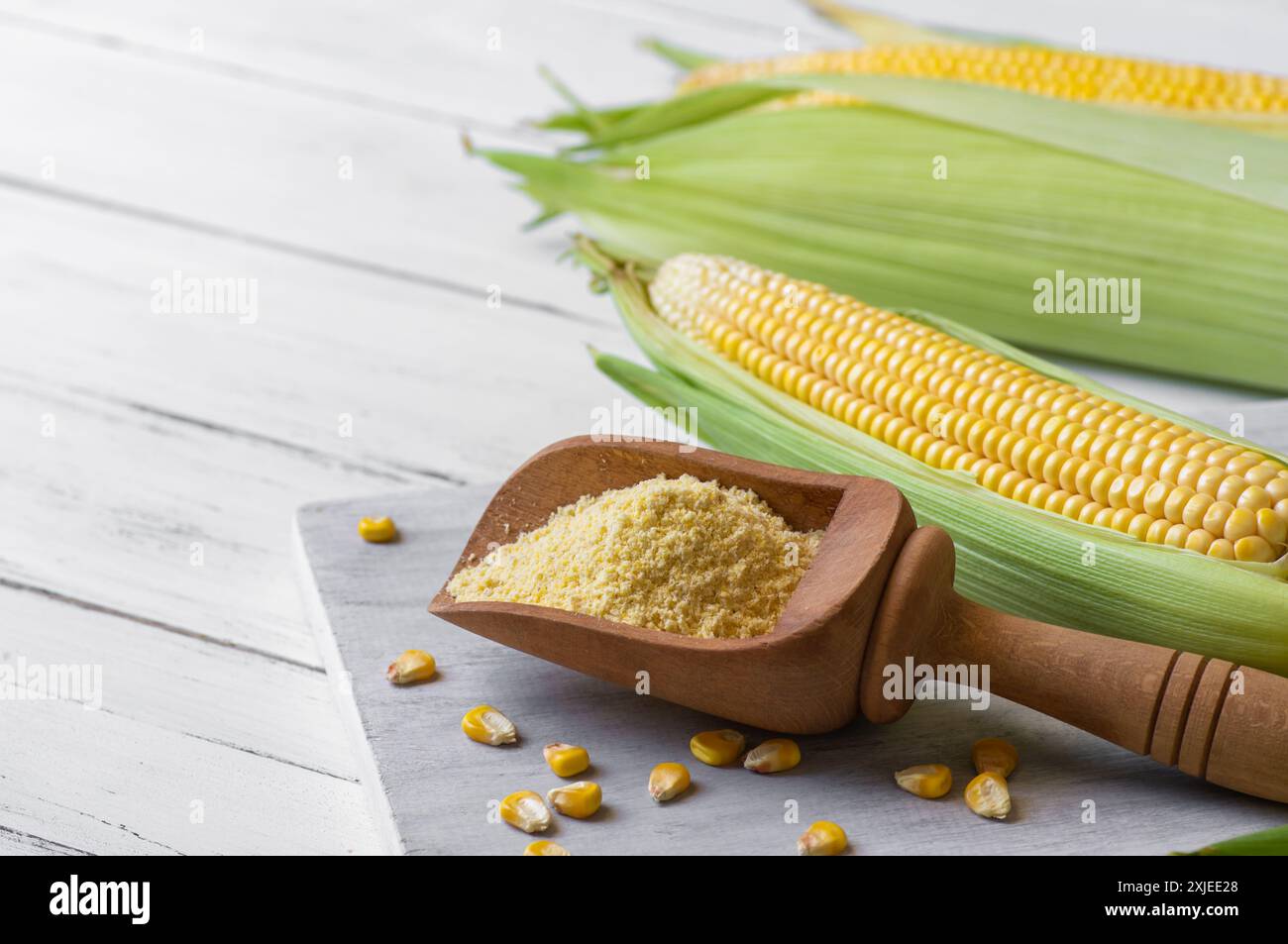 Corn flour in wooden bowl or spoon with fresh corn cobs, kernels on rustic table Stock Photo
