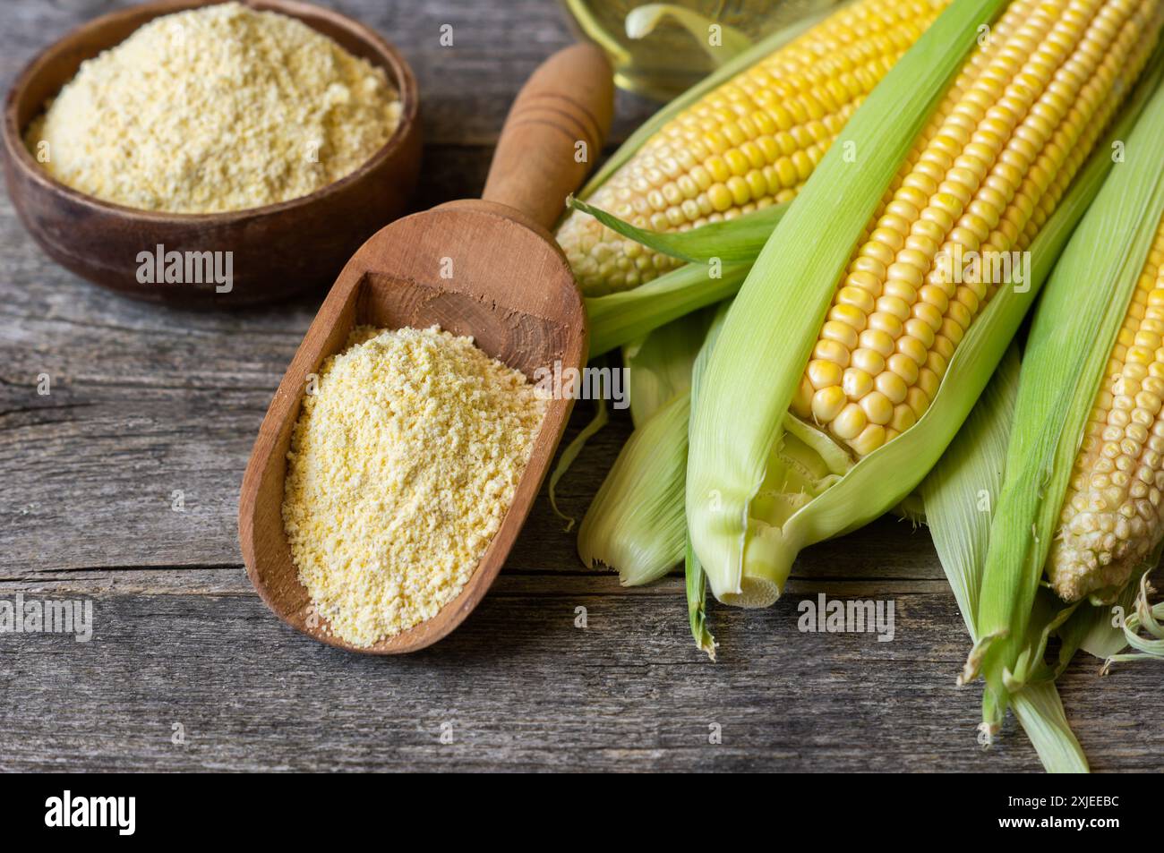 Corn flour in wooden bowl or spoon with fresh corn cobs, kernels on rustic table Stock Photo