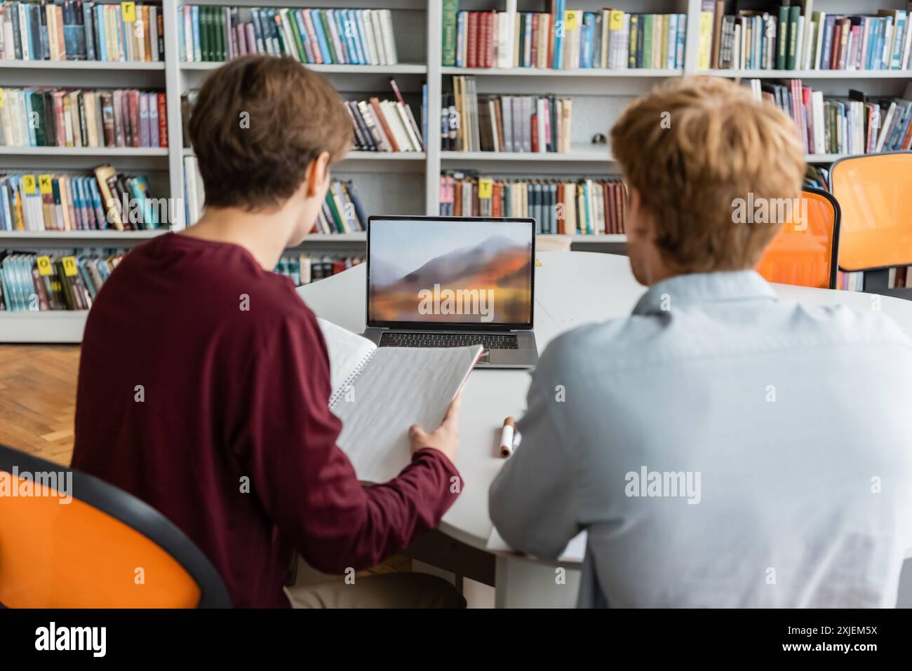 Two individuals engaged in a study session with a laptop on a table. Stock Photo