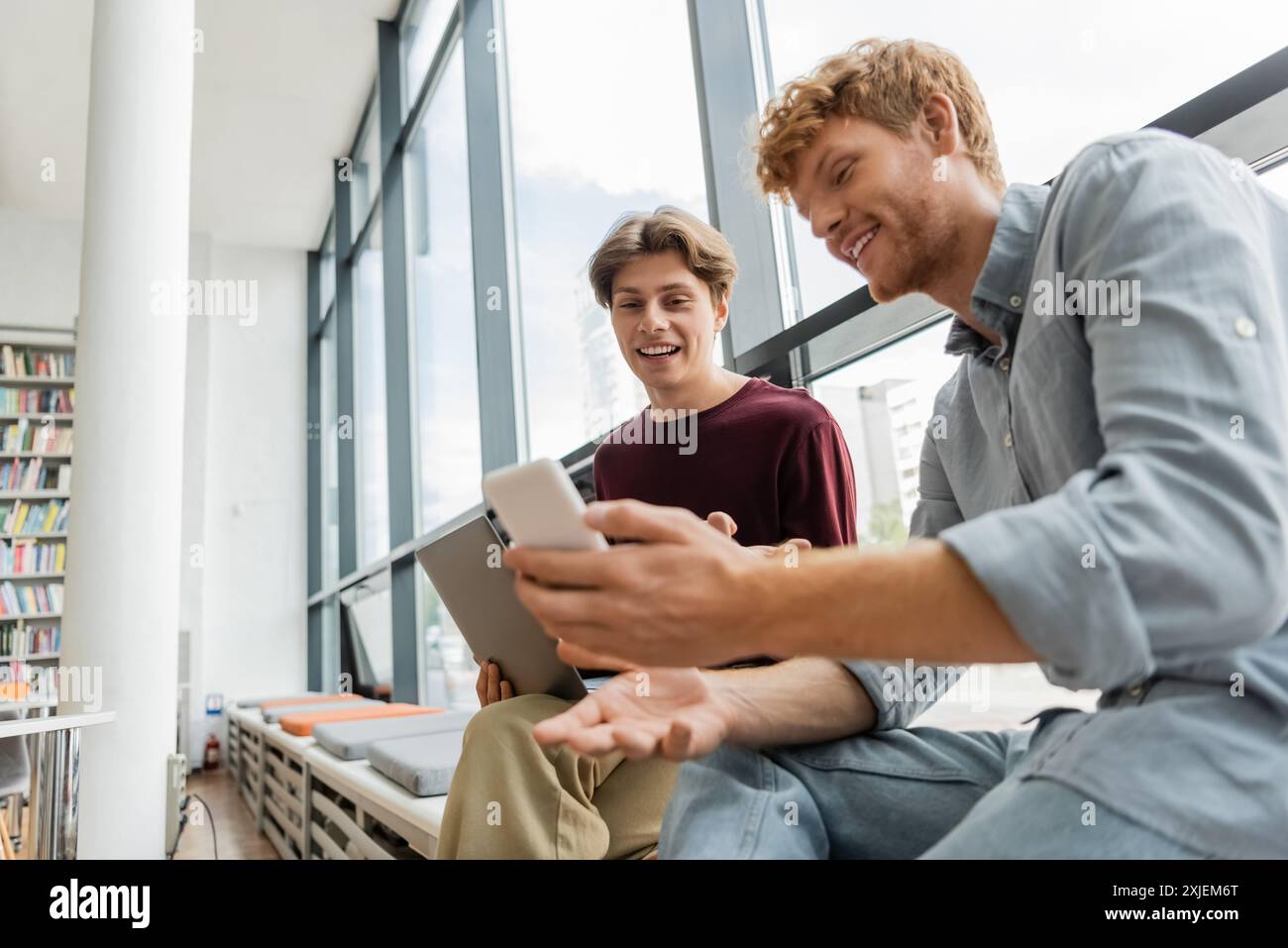 Two male students engage with a tablet while seated on the floor. Stock Photo