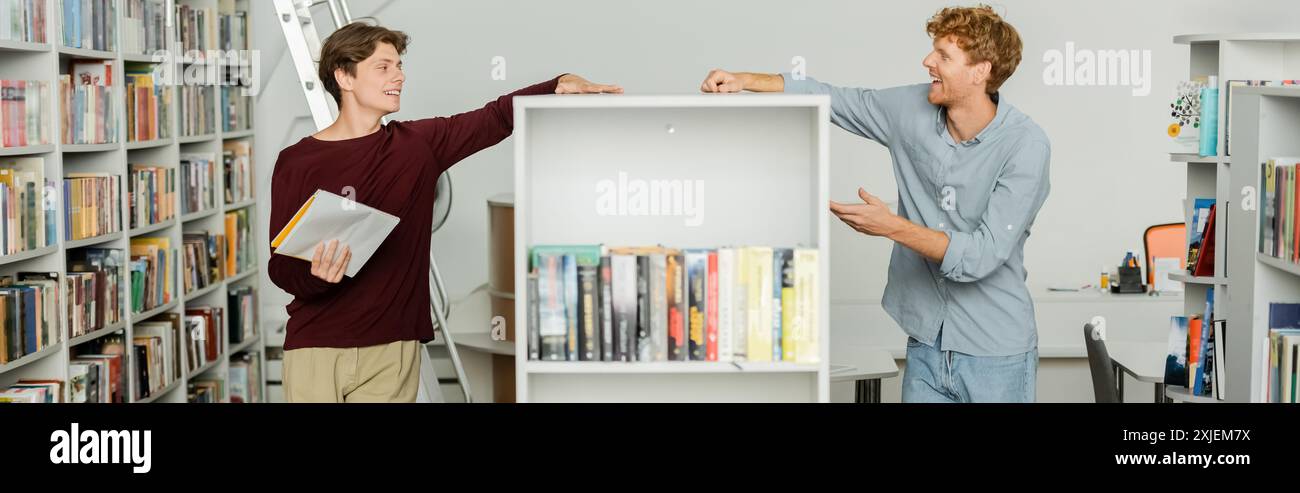 Two young students exploring books in library. Stock Photo