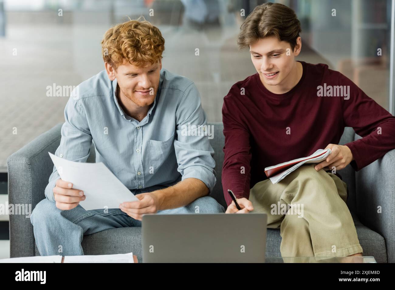 Two men engrossed in laptop work on couch. Stock Photo