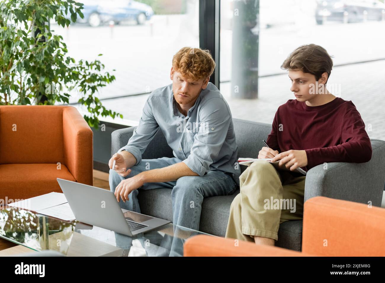 Two men engrossed in work, sitting on couches with laptops. Stock Photo