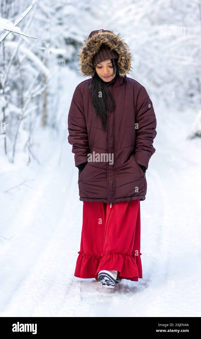 A young woman in a red suit and hooded jacket walks in a snowy forest Stock Photo