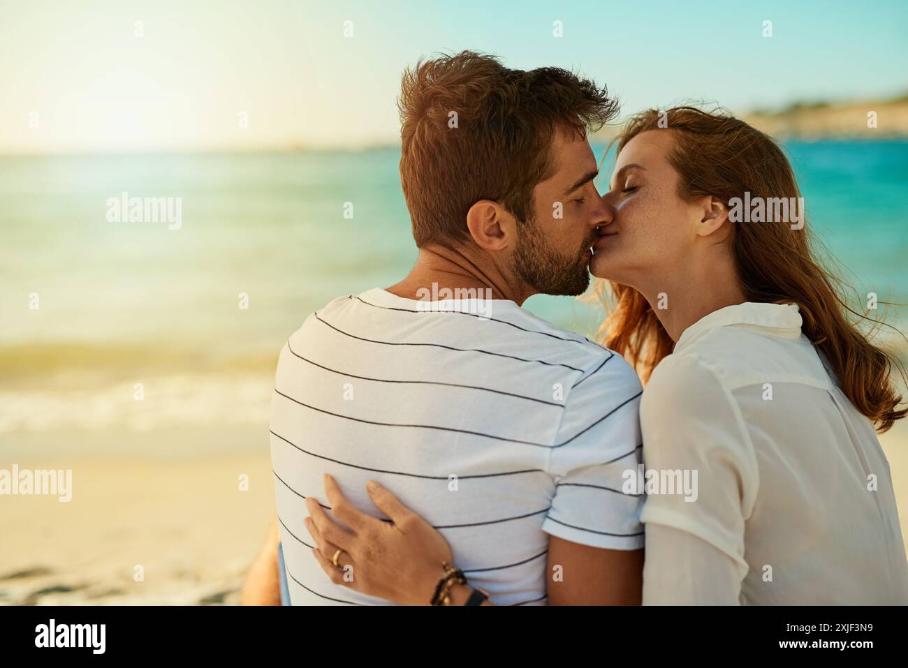 Kiss, couple and relax on beach for love, commitment and bonding on ...
