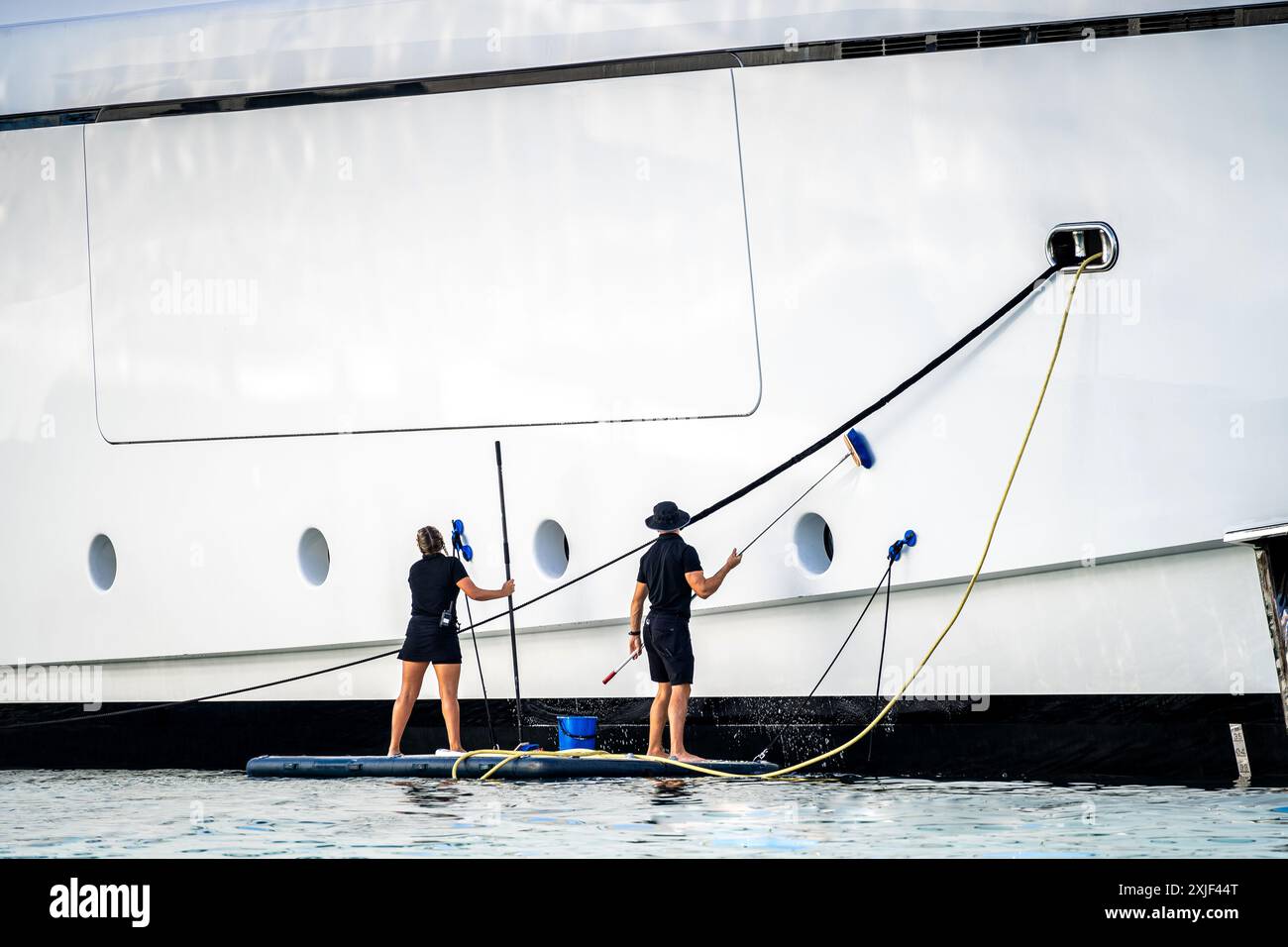 Super yacht crew, two deckhands, male and female cleaning the side of a