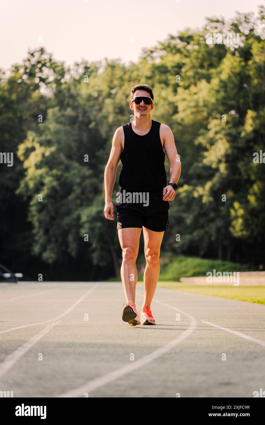 Professional athlete in training clothes smiling while walking on the track Stock Photo