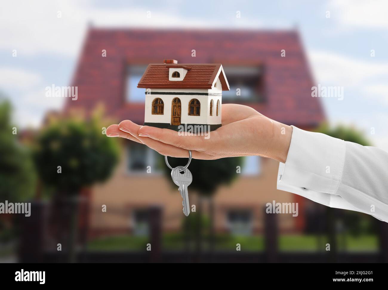 Real estate agent holding house model and key against future dwelling ...