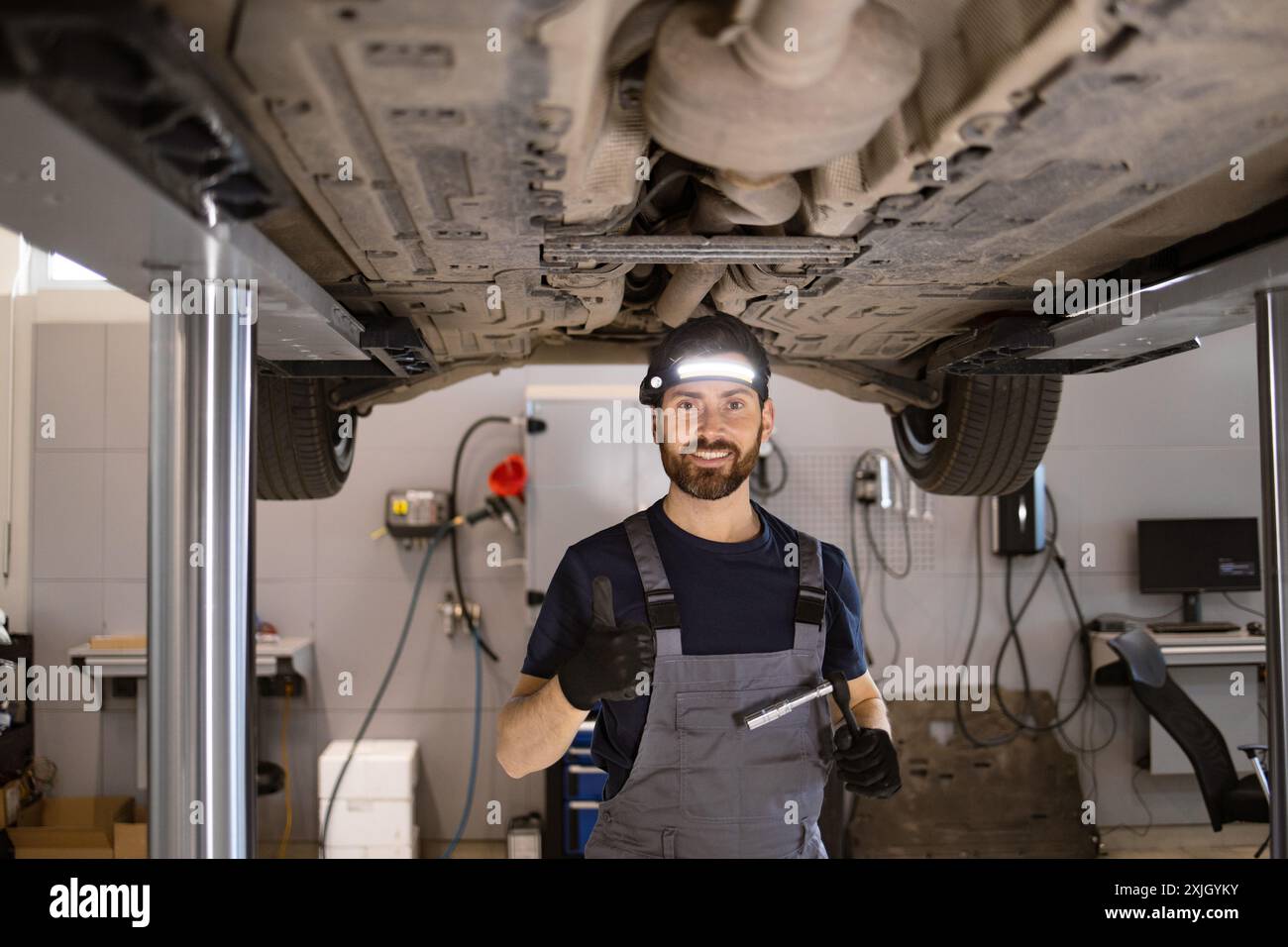 Mechanic giving thumbs up under raised car in auto repair shop Stock ...