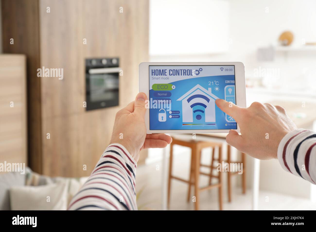 Young man with smart home security system control panel in kitchen, closeup Stock Photo