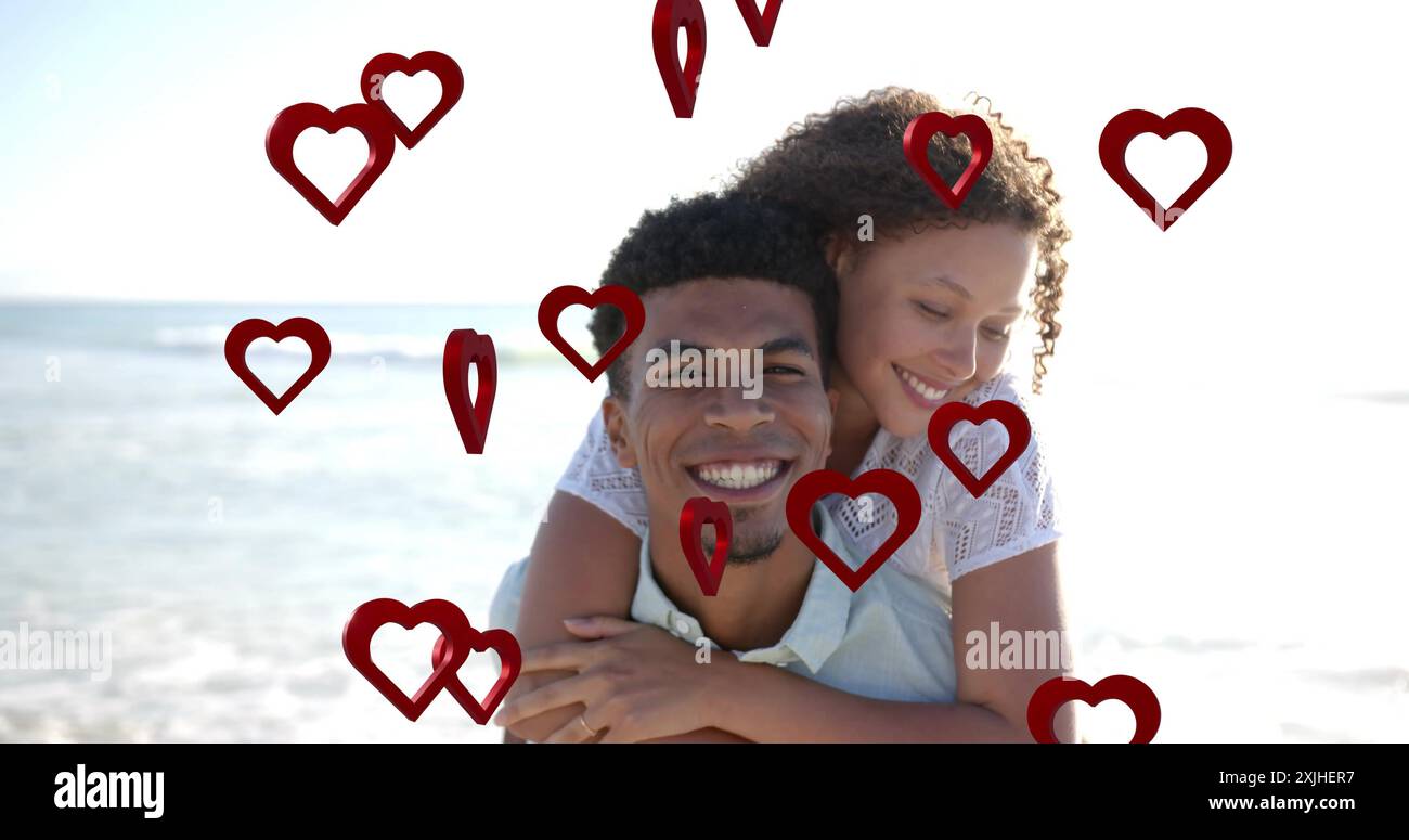 Image of hearts moving over diverse couple in love on beach in summer. Love, romance, valentine's day and vacation concept digitally generated image. Stock Photo